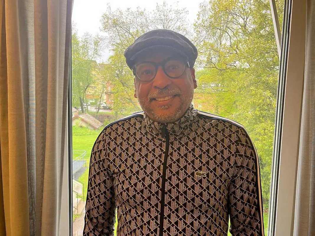 Joakim Diffang står med ryggen åt ett fönster, ler mot kameran. Han har keps och glasögon.