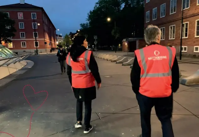 Två personer är ute i samhället med nattvandringsvästar på.