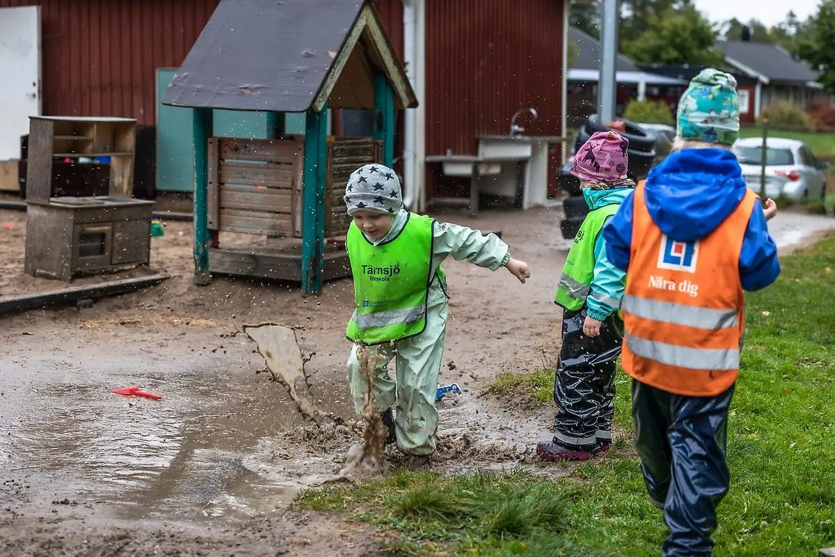 Barn i galonkläder hoppar i vattenpöl