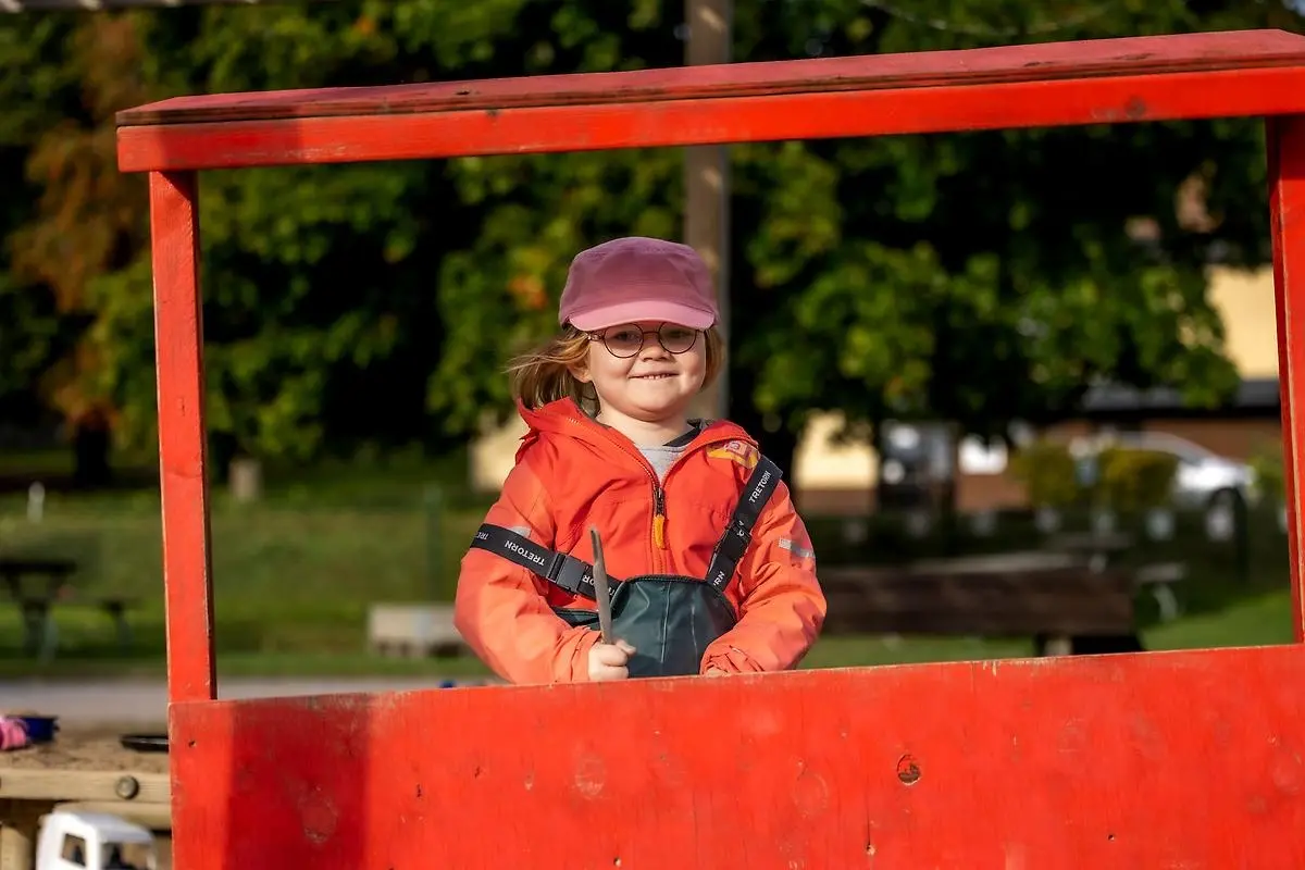 Glad flicka i förskolan i rosa keps och glasögon utomhus