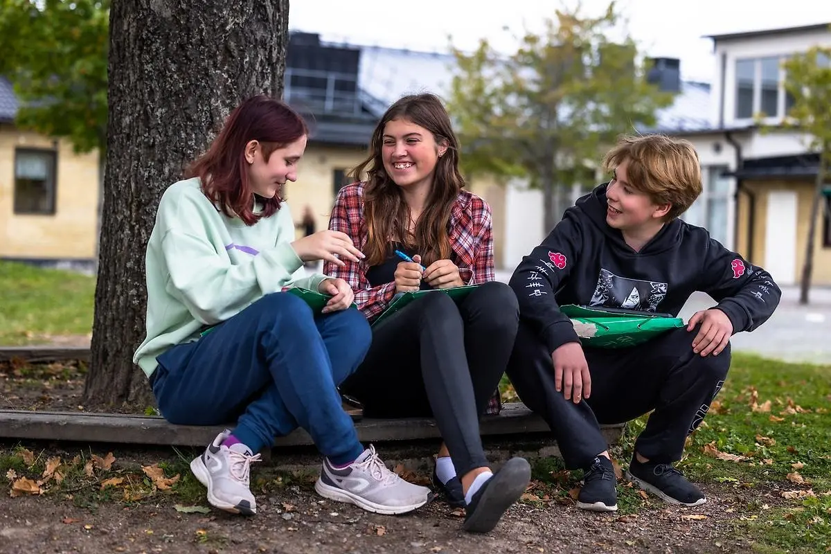 Två unga tjejer och en ung kille sitter tillsammans utomhus och skrattar