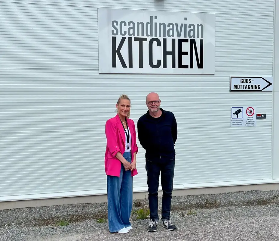 Näringslivsstrateg Maria Bergström och Thomas Strand från Nordic Kitchen group står fram för en vit byggnad med en skylt där det står Scandinavian Kitchen.