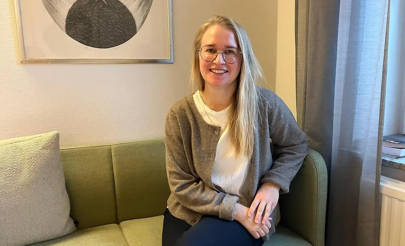 Sara Lindberg sitter i en soffa och tittar in i kameran