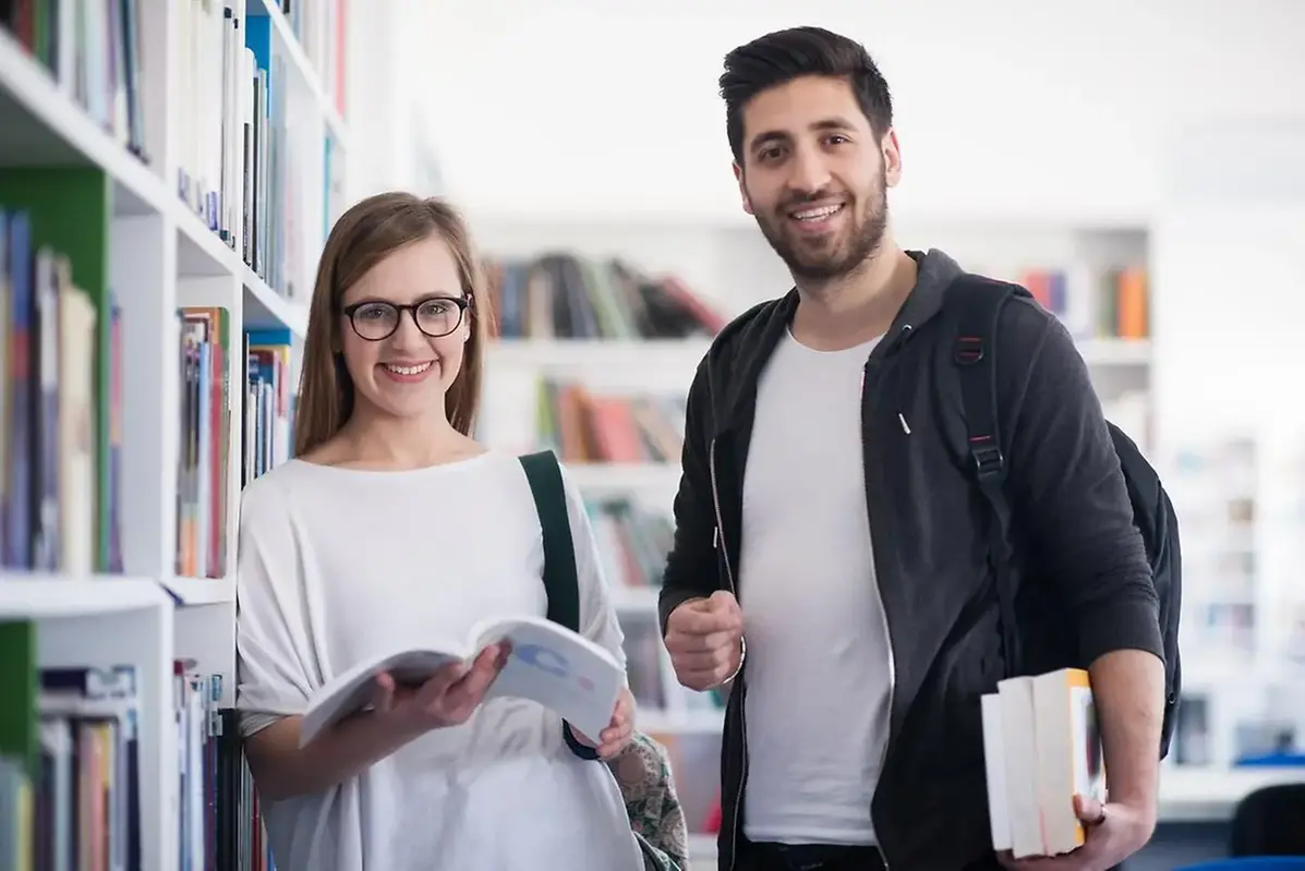 Två unga vuxna bredvid bokhylla i bibliotek