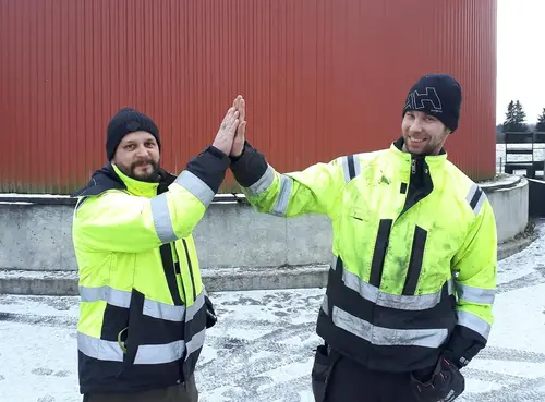 Två medarbetare gör high five. De har varseljackor på. 