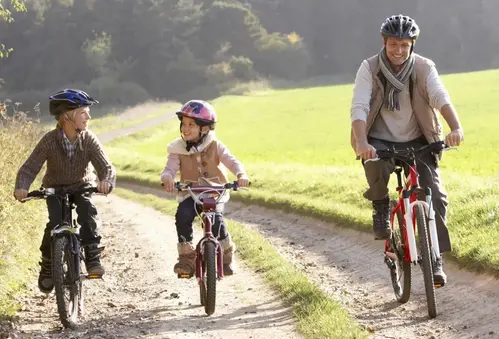 Pappa cyklar med sina två barn på en landsväg