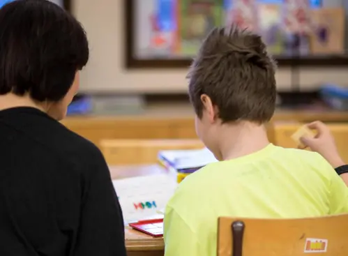Pedagog och elev sitter med ryggarna till vid ett bord och arbetar