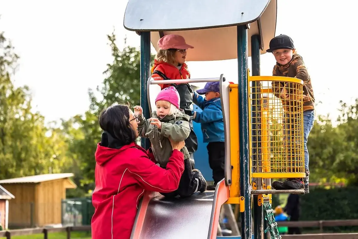 Förskolelärare tillsammans med många barn vid klätterställning