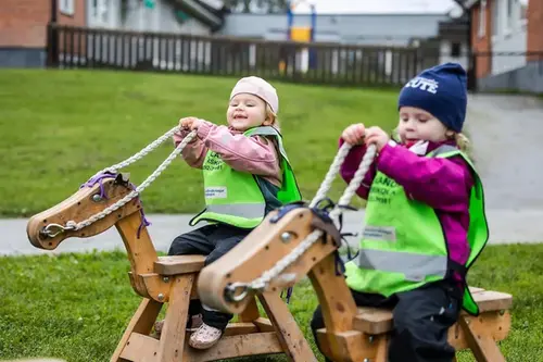 Två förskolebarn rider på låtsashästar utomhus